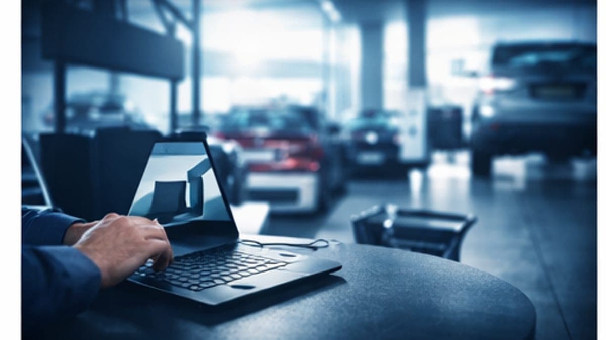 A motor trader reviewing service history records on a laptop at a car dealership